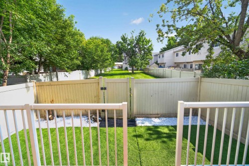 Fenced backyard featuring artificial turf, white gravel accents, and a gate opening to a grassy common area - 175 Centennial Crest Nw, Edmonton, AB - Outdoor With Deck Patio Veranda