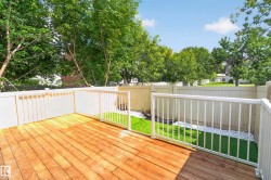Expansive wood-finish deck with white railings, a fenced perimeter, and a landscaped area featuring artificial turf and white decorative stones - 