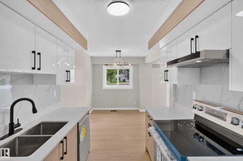 Gourmet kitchen featuring sleek white cabinetry, light countertops, integrated stainless steel appliances, and wood-finish flooring - 175 Centennial Crest Nw, Edmonton, AB - Indoor Photo Showing Kitchen With Double Sink With Upgraded Kitchen