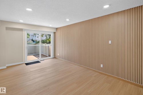 Recessed lighting, wood-finish flooring, accent wall with vertical paneling, sliding glass door, and private balcony - 175 Centennial Crest Nw, Edmonton, AB - Indoor Photo Showing Other Room