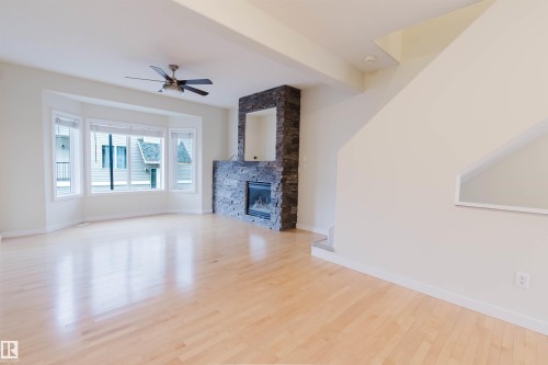 Hardwood flooring, bay window, stone-clad fireplace with mantel, built-in electric fireplace, and ceiling fan - #2 13215 153 Av Nw, Edmonton, AB - Indoor With Fireplace