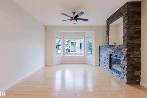 Hardwood flooring, bay window, stone-clad fireplace with insert, and ceiling fan - #2 13215 153 Av Nw, Edmonton, AB - Indoor Photo Showing Living Room With Fireplace