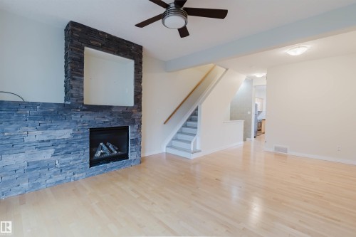 Hardwood-finish flooring, stone-clad fireplace with mantel niche, gas insert fireplace, ceiling fan with integrated lighting, and a staircase with a wood handrail - #2 13215 153 Av Nw, Edmonton, AB - Indoor Photo Showing Living Room With Fireplace