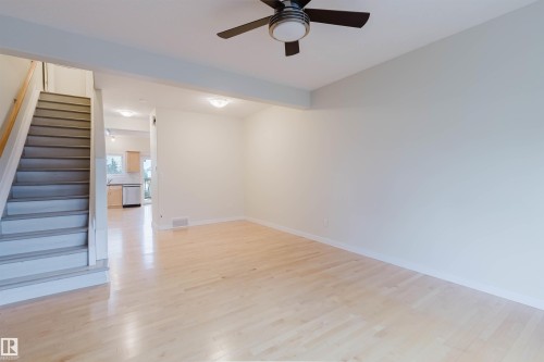 Light wood-finish flooring, staircase with wood handrail, ceiling-mounted fan with integrated lighting, recessed ceiling lighting, and a kitchen with light wood cabinetry and a stainless steel appliance - #2 13215 153 Av Nw, Edmonton, AB - Indoor Photo Showing Other Room