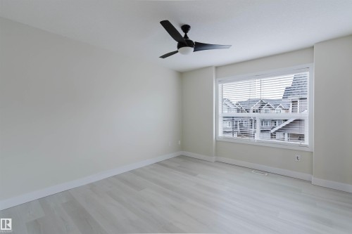 Light-toned wood-finish flooring, ceiling fan with integrated lighting, expansive window with horizontal blinds, and neutral wall paint - #2 13215 153 Av Nw, Edmonton, AB - Indoor Photo Showing Other Room