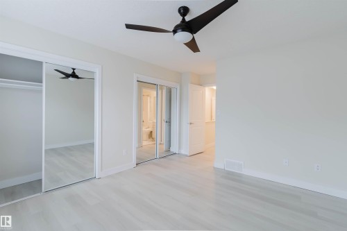 Light wood-finish flooring, modern ceiling fan with integrated lighting, and multiple mirrored sliding closet doors - #2 13215 153 Av Nw, Edmonton, AB - Indoor Photo Showing Other Room
