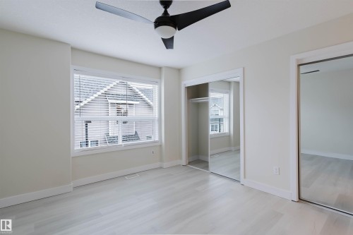 White-painted room with wood-finish flooring, a ceiling fan, and two mirrored closet doors - #2 13215 153 Av Nw, Edmonton, AB - Indoor Photo Showing Other Room