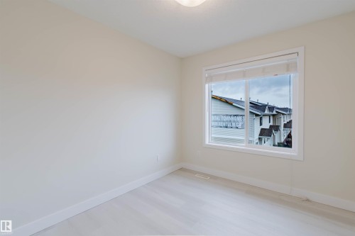 Light-toned wood-finish flooring, neutral wall paint, and a large window with white trim - #2 13215 153 Av Nw, Edmonton, AB - Indoor Photo Showing Other Room