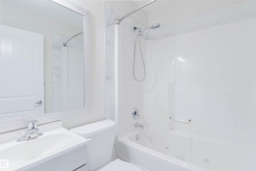 Vanity with integrated sink, chrome faucet, framed mirror, toilet, and jetted tub - #2 13215 153 Av Nw, Edmonton, AB - Indoor Photo Showing Bathroom