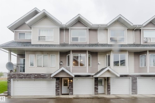 Multi-unit structure with varied siding, multiple window styles, integrated garage doors, and stone-finish accents - #2 13215 153 Av Nw, Edmonton, AB - Outdoor With Facade