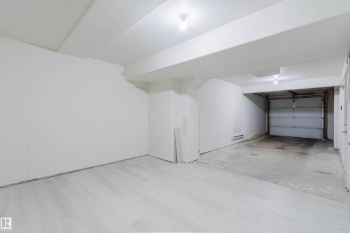 Open garage space featuring a roll-up door, concrete flooring, and light-toned wood-finish flooring in the adjacent area - #2 13215 153 Av Nw, Edmonton, AB - Indoor Photo Showing Garage