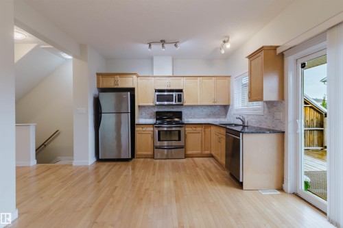 Kitchen featuring wood-finish cabinetry, stainless steel appliances, dark countertops, and a patterned tile backsplash - #2 13215 153 Av Nw, Edmonton, AB - Indoor Photo Showing Kitchen With Stainless Steel Kitchen
