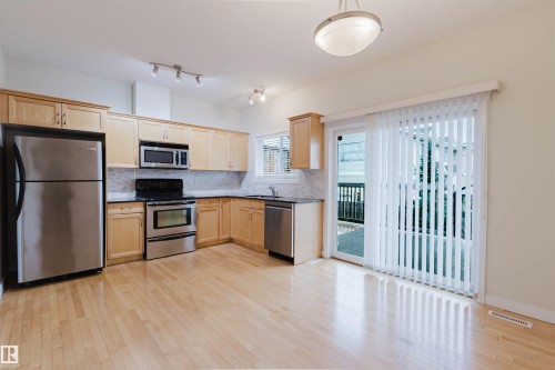 Kitchen featuring light wood-finish cabinetry, stainless steel appliances, and wood-finish flooring - #2 13215 153 Av Nw, Edmonton, AB - Indoor Photo Showing Kitchen With Stainless Steel Kitchen