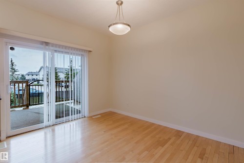 Light wood-finish flooring, neutral wall tones, semi-flush mount lighting, and sliding glass door access to an outdoor deck with wood and wrought iron railings - #2 13215 153 Av Nw, Edmonton, AB - Indoor Photo Showing Other Room