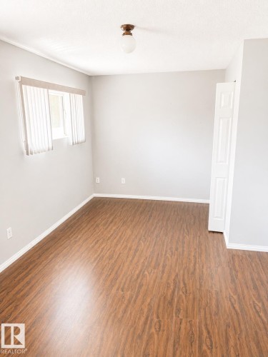 Wood-finish flooring, light gray wall tones, ceiling-mounted light fixture, white vertical blinds, and white trim accents - 802 16 Avenue, Cold Lake, AB - Indoor Photo Showing Other Room