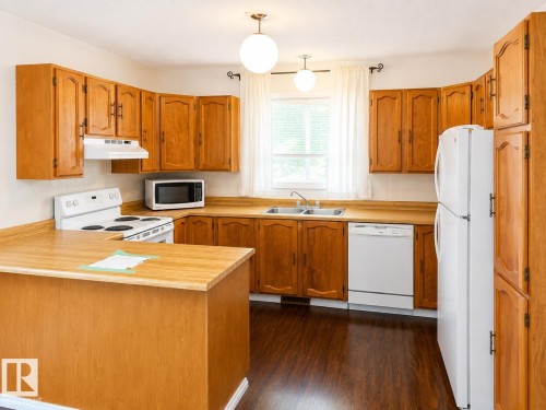 Kitchen featuring wood-finish cabinetry, a built-in double basin sink, white appliances, and wood-finish flooring - 802 16 Avenue, Cold Lake, AB - Indoor Photo Showing Kitchen With Double Sink