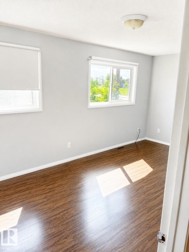 Wood-finish flooring, light gray wall paint, two windows, and a ceiling-mounted light fixture - 802 16 Avenue, Cold Lake, AB - Indoor Photo Showing Other Room