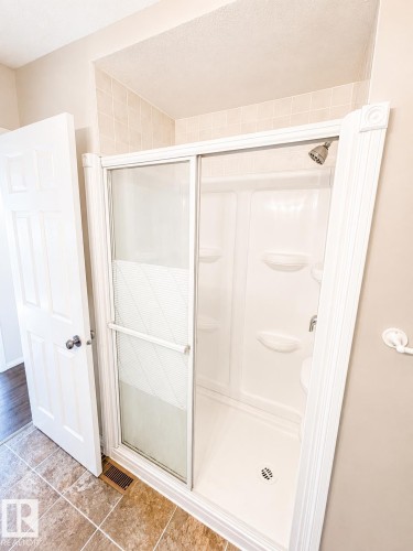 White-framed shower with sliding glass doors, integrated shelving, and a brushed metal shower head - 802 16 Avenue, Cold Lake, AB - Indoor Photo Showing Bathroom