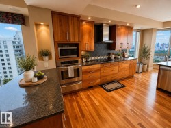 Built-in stainless steel appliances, wood cabinetry, dark stone countertops, wood-finish flooring, and a tiled backsplash - 