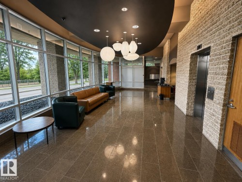 Expansive floor-to-ceiling windows, polished tile flooring, textured brick wall, modern pendant lighting, and a built-in elevator - #1201 10035 Saskatchewan Dr Nw, Edmonton, AB - Indoor Photo Showing Other Room