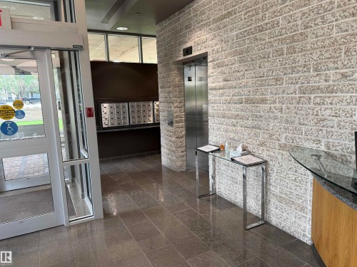 Entry foyer with automatic glass doors, tiled flooring, textured brick-finish walls, and a stainless steel elevator - #1201 10035 Saskatchewan Dr Nw, Edmonton, AB -  Photo Showing Other Room