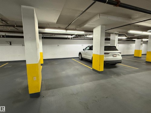 Underground parking space with concrete flooring, illuminated by overhead lighting, featuring numbered parking spots, and structural support columns - #1201 10035 Saskatchewan Dr Nw, Edmonton, AB - Indoor Photo Showing Garage