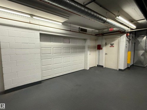 White paneled garage door, painted concrete block walls, and overhead fluorescent lighting - #1201 10035 Saskatchewan Dr Nw, Edmonton, AB - Indoor Photo Showing Basement