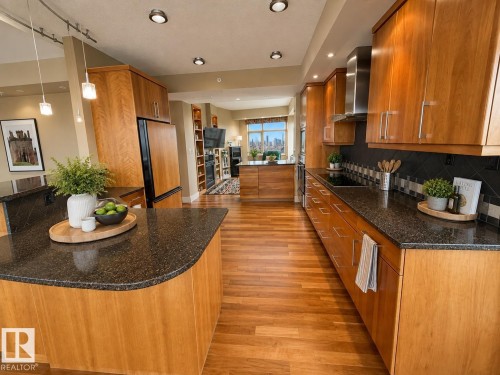 Kitchen featuring wood-finish flooring, dark stone countertops, wood cabinetry, stainless steel appliances, and recessed lighting - #1201 10035 Saskatchewan Dr Nw, Edmonton, AB - Indoor Photo Showing Kitchen