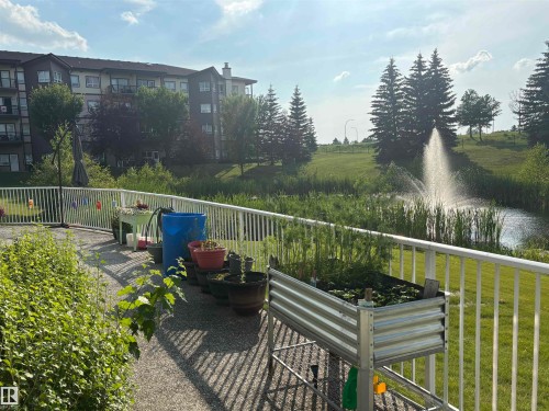 Private balcony featuring a white railing, overlooking a pond with a fountain and mature trees - #202 8802 Southfort Dr, Fort Saskatchewan, AB - Outdoor