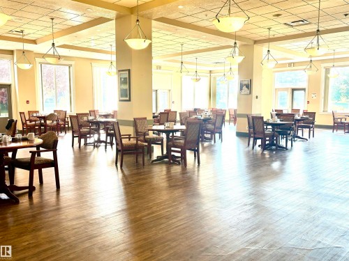 Spacious dining area featuring wood-finish flooring, abundant natural light from multiple large windows, and a dropped ceiling with recessed lighting - #202 8802 Southfort Dr, Fort Saskatchewan, AB - Indoor