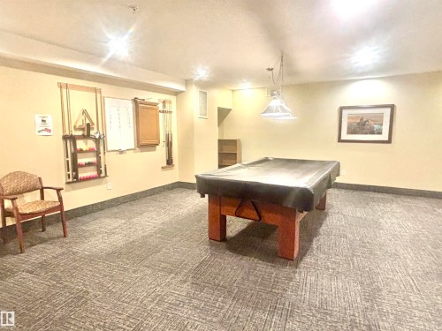 Recreation room featuring a pool table with cover, wall-mounted cue rack, pendant lighting, and pattern carpet flooring - #202 8802 Southfort Dr, Fort Saskatchewan, AB - Indoor Photo Showing Other Room
