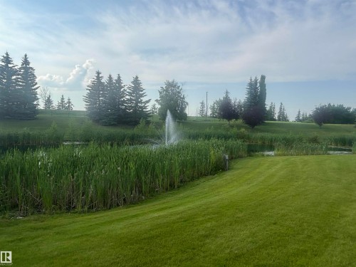 Expansive lawn area bordering a tranquil pond with a central fountain - #202 8802 Southfort Dr, Fort Saskatchewan, AB - Outdoor With View