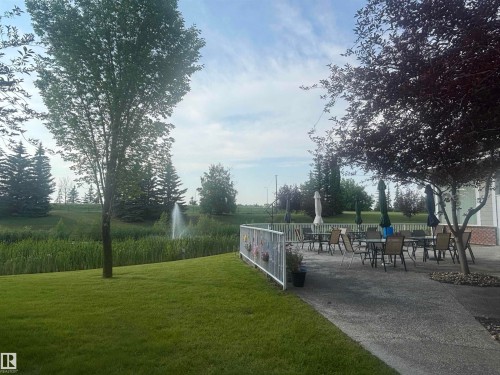 Patio dining area featuring multiple tables and chairs, a concrete surface, and mature trees providing shade - #202 8802 Southfort Dr, Fort Saskatchewan, AB - Outdoor