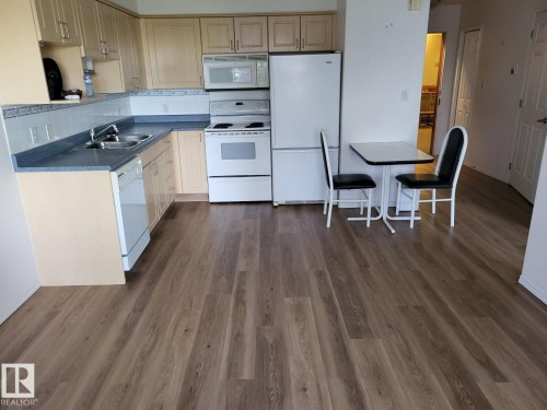Kitchen featuring wood-finish flooring, light-toned cabinetry, a blue countertop, a white tile backsplash, and white appliances - #202 8802 Southfort Dr, Fort Saskatchewan, AB - Indoor Photo Showing Kitchen With Double Sink