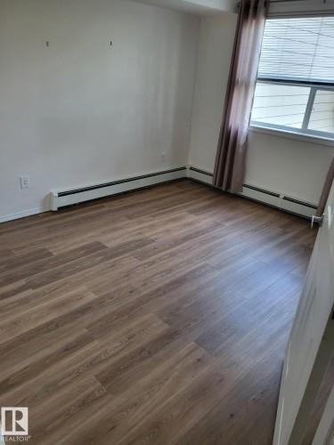 Spacious room featuring wood-finish flooring, white walls, and a window with blinds - #202 8802 Southfort Dr, Fort Saskatchewan, AB - Indoor Photo Showing Other Room