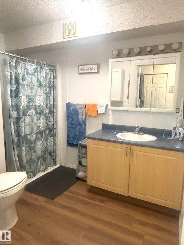 Bathroom featuring wood-finish flooring, a light wood vanity with a single sink, and a mirrored medicine cabinet with integrated lighting - #202 8802 Southfort Dr, Fort Saskatchewan, AB - Indoor Photo Showing Bathroom