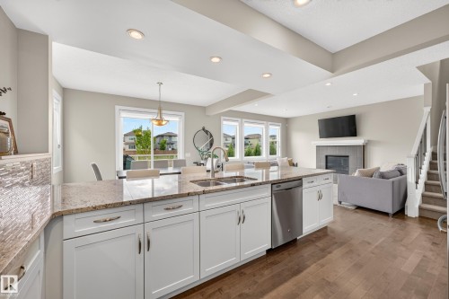 Open-concept kitchen with a large island, white cabinetry, integrated stainless steel dishwasher, and a double basin sink - 1323 158 Street Sw, Edmonton, AB - Indoor Photo Showing Kitchen With Fireplace With Double Sink With Upgraded Kitchen