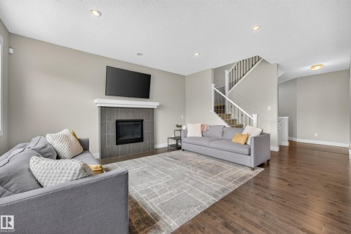 Living area featuring a tiled fireplace with mantel, dark wood-finish flooring, recessed lighting, and a staircase with white spindles - 1323 158 Street Sw, Edmonton, AB - Indoor Photo Showing Living Room With Fireplace