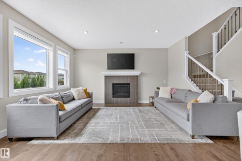 Spacious living area featuring wood-finish flooring, a fireplace with a tile surround and mantel, abundant natural light through multiple windows, and a carpeted staircase with white railings - 1323 158 Street Sw, Edmonton, AB - Indoor Photo Showing Living Room With Fireplace