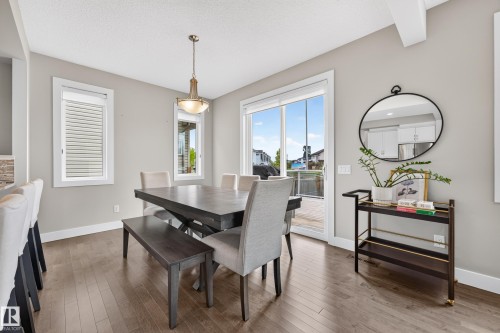 Open-concept dining area featuring wood-finish flooring, a contemporary chandelier, multiple windows, and a sliding glass door leading to an outdoor space - 1323 158 Street Sw, Edmonton, AB - Indoor Photo Showing Dining Room