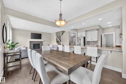 Open concept living space featuring wood-finish flooring, a kitchen island with seating, white cabinetry, a tiled backsplash, and a fireplace with a mantel - 1323 158 Street Sw, Edmonton, AB - Indoor Photo Showing Dining Room