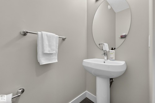 Pedestal sink with chrome-finish faucet, an oval-shaped mirror, and light gray wall paint - 1323 158 Street Sw, Edmonton, AB - Indoor Photo Showing Bathroom