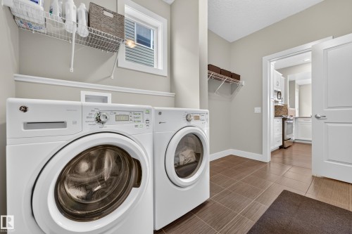 Dedicated laundry area featuring a front-load washer and dryer, wire shelving, a window, and tile flooring - 1323 158 Street Sw, Edmonton, AB - Indoor Photo Showing Laundry Room