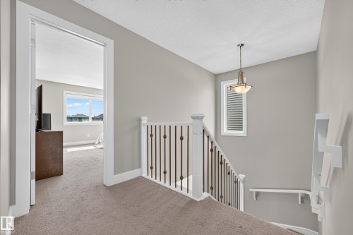 Carpeted landing featuring a white railing with dark metal balusters, a window with horizontal blinds, and a suspended ceiling light fixture - 1323 158 Street Sw, Edmonton, AB - Indoor Photo Showing Other Room