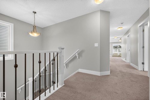 Upper landing featuring neutral carpeting, a staircase with wrought iron balusters, a decorative pendant light fixture, and recessed lighting in the hallway - 1323 158 Street Sw, Edmonton, AB - Indoor Photo Showing Other Room