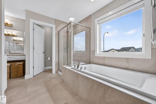 Freestanding soaking tub with tiled surround, glass-enclosed shower, large window, and double vanity with built-in cabinetry - 1323 158 Street Sw, Edmonton, AB - Indoor Photo Showing Bathroom