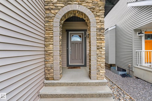 Arched stone entry with a paneled front door, concrete porch, and matching concrete steps - 1323 158 Street Sw, Edmonton, AB - Outdoor