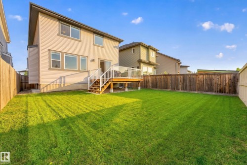 Expansive backyard featuring a manicured lawn, a raised wood deck with glass railing, and wood privacy fencing - 1323 158 Street Sw, Edmonton, AB - Outdoor With Deck Patio Veranda With Backyard With Exterior