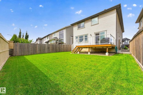 Expansive backyard featuring a manicured lawn, full privacy fencing, and a wooden deck with glass panel railing - 1323 158 Street Sw, Edmonton, AB - Outdoor With Deck Patio Veranda With Exterior