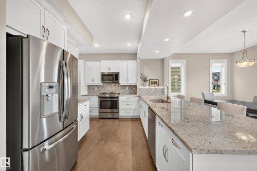Kitchen featuring stainless steel appliances, white cabinetry, a stone-finish countertop island, wood-finish flooring, and recessed lighting - 1323 158 Street Sw, Edmonton, AB - Indoor Photo Showing Kitchen With Stainless Steel Kitchen With Upgraded Kitchen
